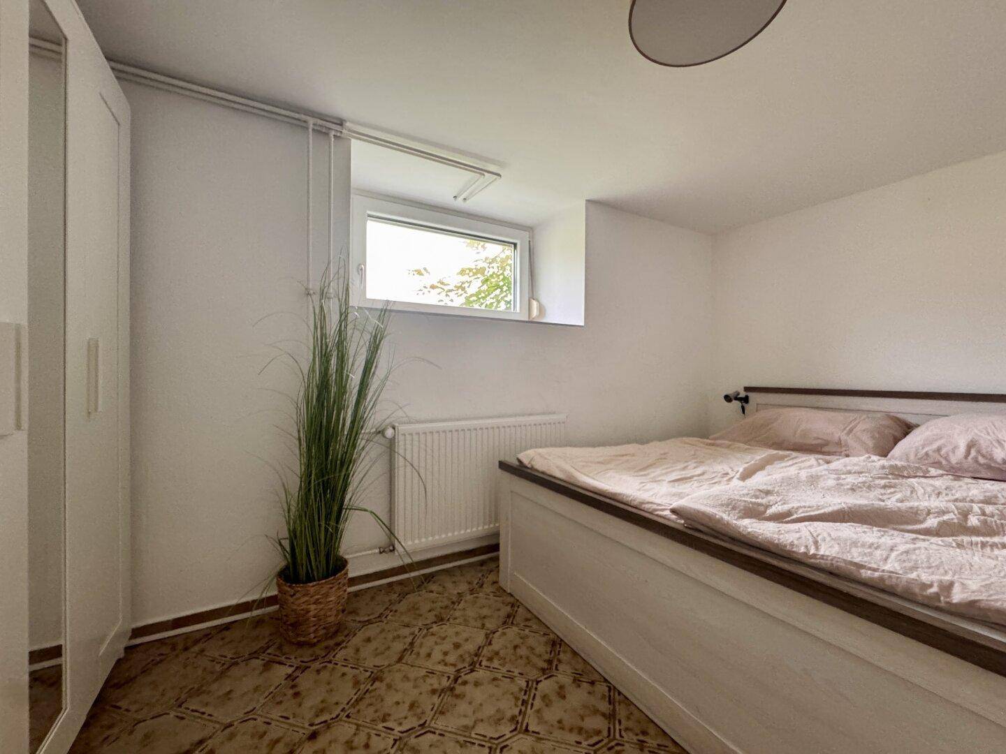 Schlafzimmer im Untergeschoss mit Bett, Kleiderschrank und einem kleinen, hochgelegenen Fenster.