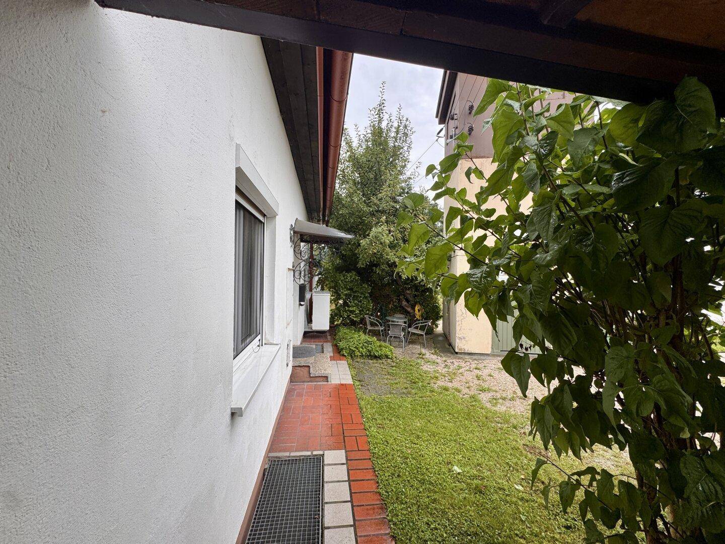 Seitenansicht des Hauses mit gepflastertem Weg und grüner Bepflanzung.