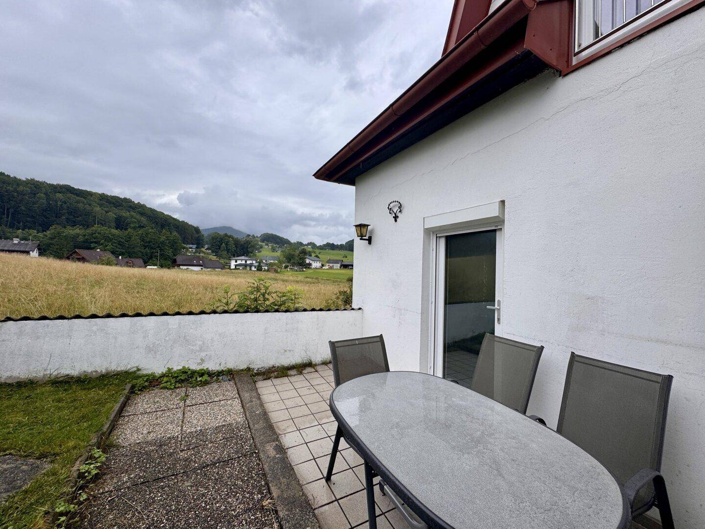 Gemütliche Terrasse mit Gartenmöbeln und weitem Blick über Felder und grüne Hügel.
