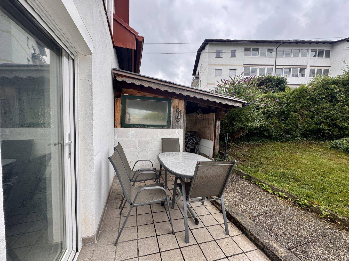 Terrasse mit Sitzgelegenheiten neben dem Haus und einem kleinen Holzschuppen im Gartenbereich.