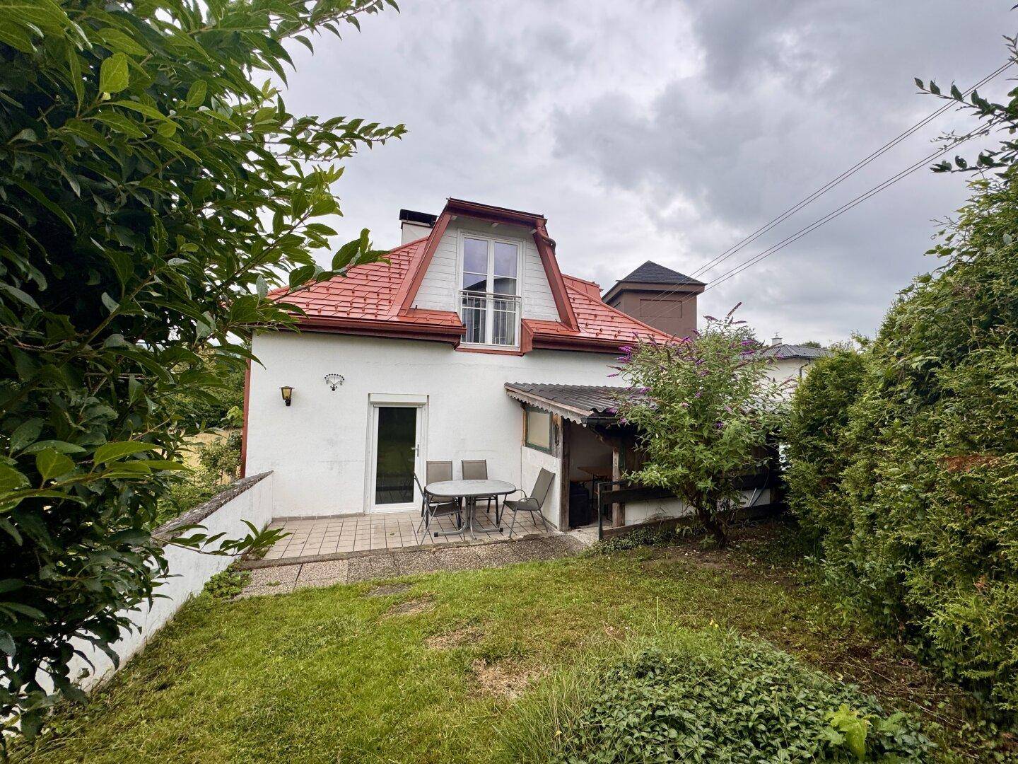 Rückansicht des Hauses mit Terrasse, Gartenbereich und einem kleinen Balkon im Obergeschoss.