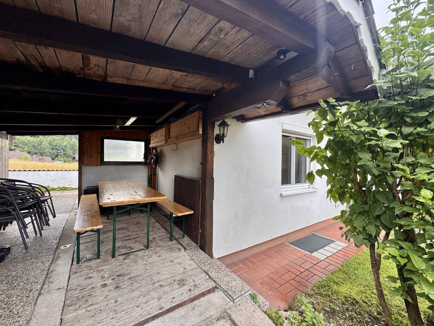 Überdachter Außenbereich mit Holztisch und Bänken, ideal für gesellige Stunden im Freien.