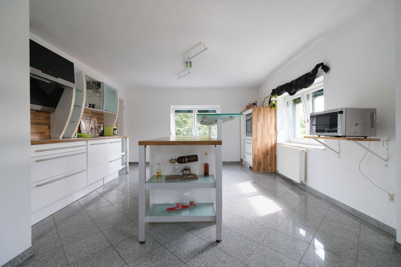 Geräumige Küche mit Kücheninsel, Fliesenboden und viel Tageslicht durch Fenster.