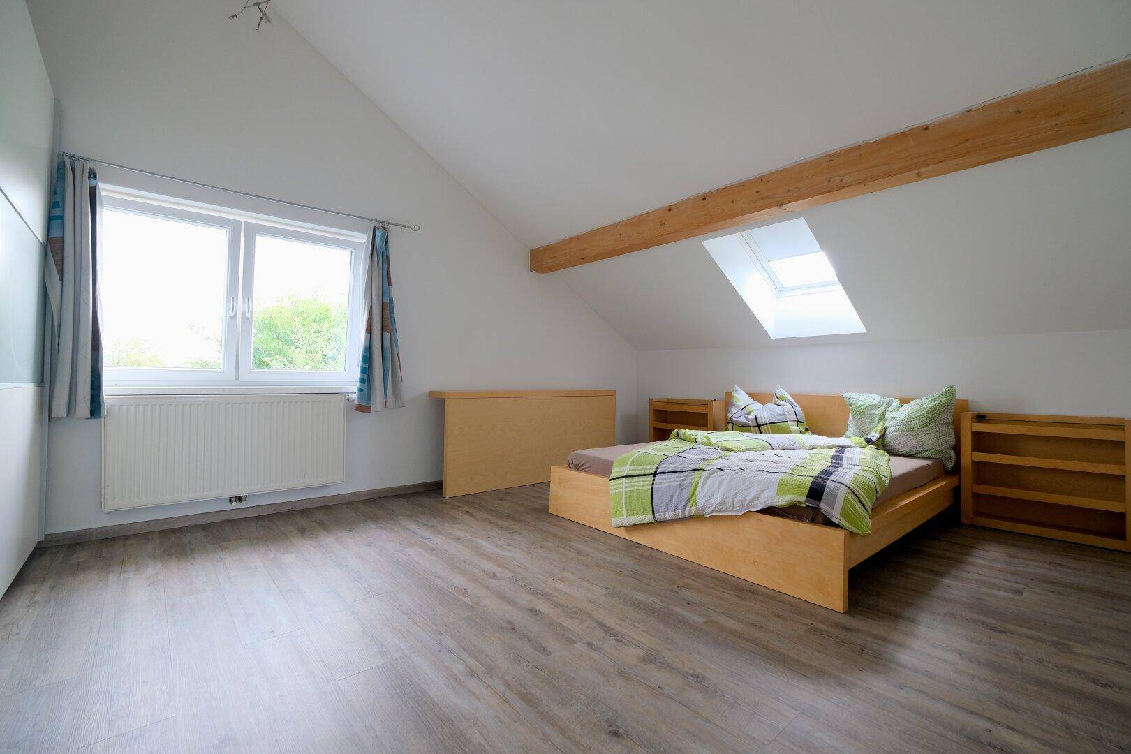 Schlafzimmer im Dachgeschoss mit Holzbalken, Dachfenster und Laminatboden.