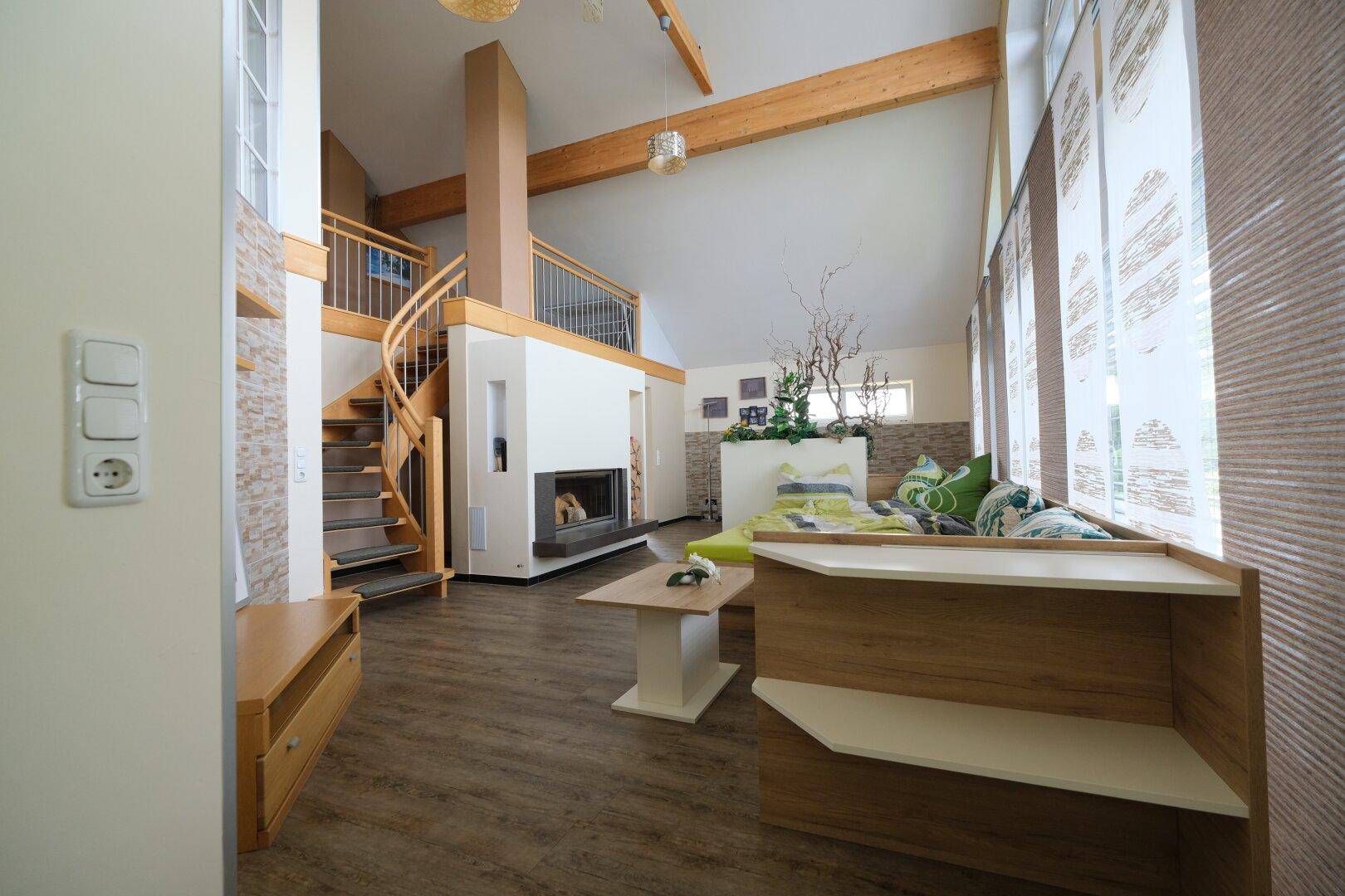 Geräumiges Wohnzimmer mit hohen Decken, Holzbalken, Kamin und Wendeltreppe.