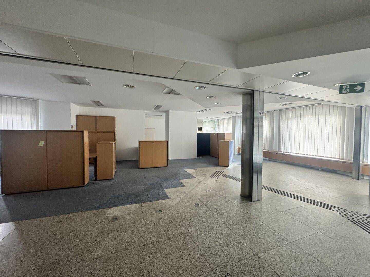 Großer, offener Bürobereich mit Teppich- und Fliesenboden, ausgestattet mit mobilen Trennwänden und viel Tageslicht.
