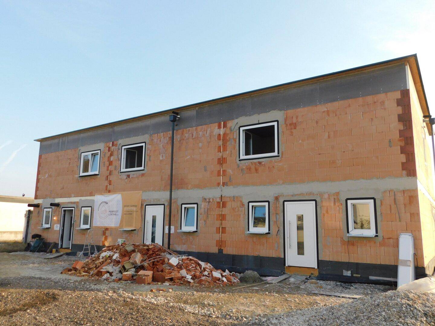 Rückansicht des Reihenhauses im Rohbau mit Ziegelmauerwerk und vorbereiteten Fenster- und Türöffnungen.
