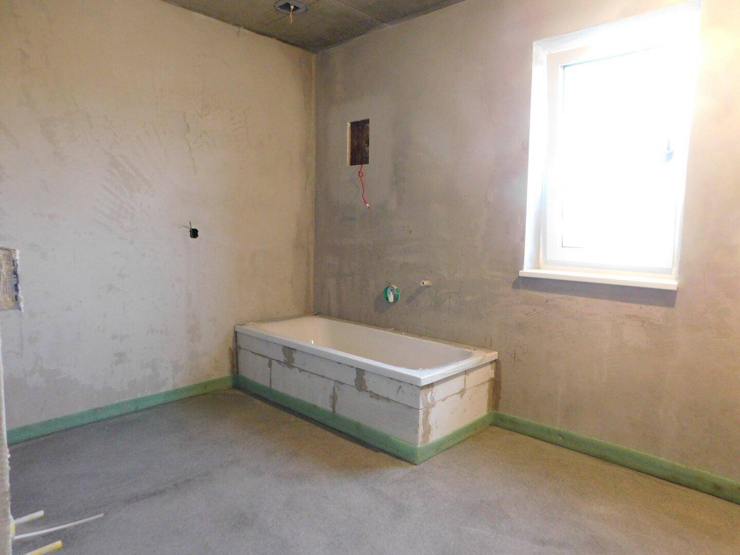 Badezimmer im Rohbau mit eingebauter Badewanne und Fenster, bereit für den weiteren Ausbau.