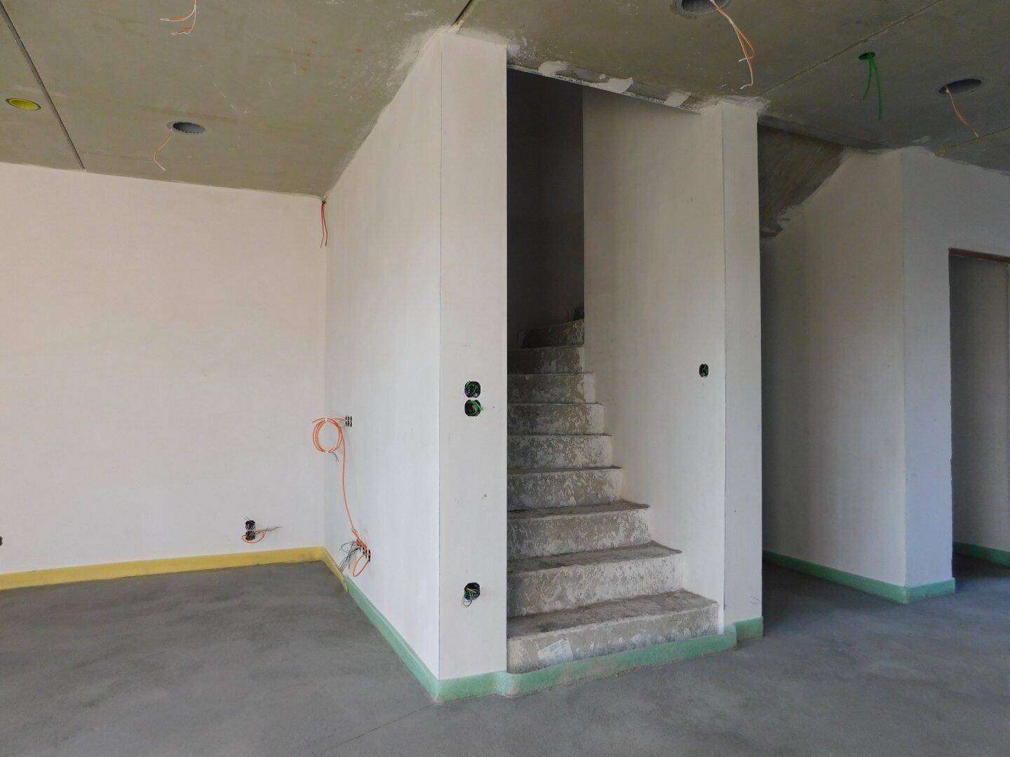 Raum im Rohbau mit Betondecke und Treppenaufgang, bereit für den weiteren Ausbau.