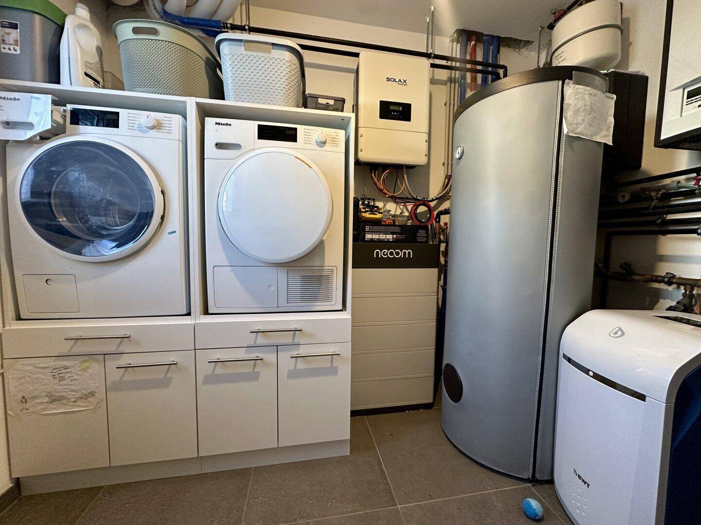 Hauswirtschaftsraum mit Waschmaschine, Trockner, Warmwasserspeicher und Photovoltaik-Systemkomponenten.