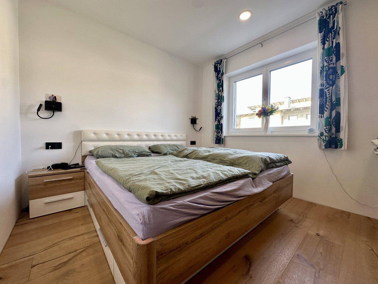 Helles Schlafzimmer mit Doppelbett, Holzboden und einem großen Fenster.