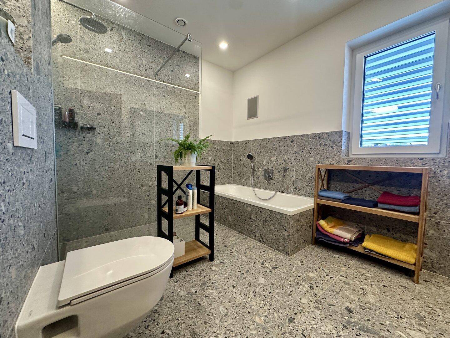 Modernes Badezimmer mit grauen Terrazzo-Fliesen, begehbarer Dusche und Badewanne.