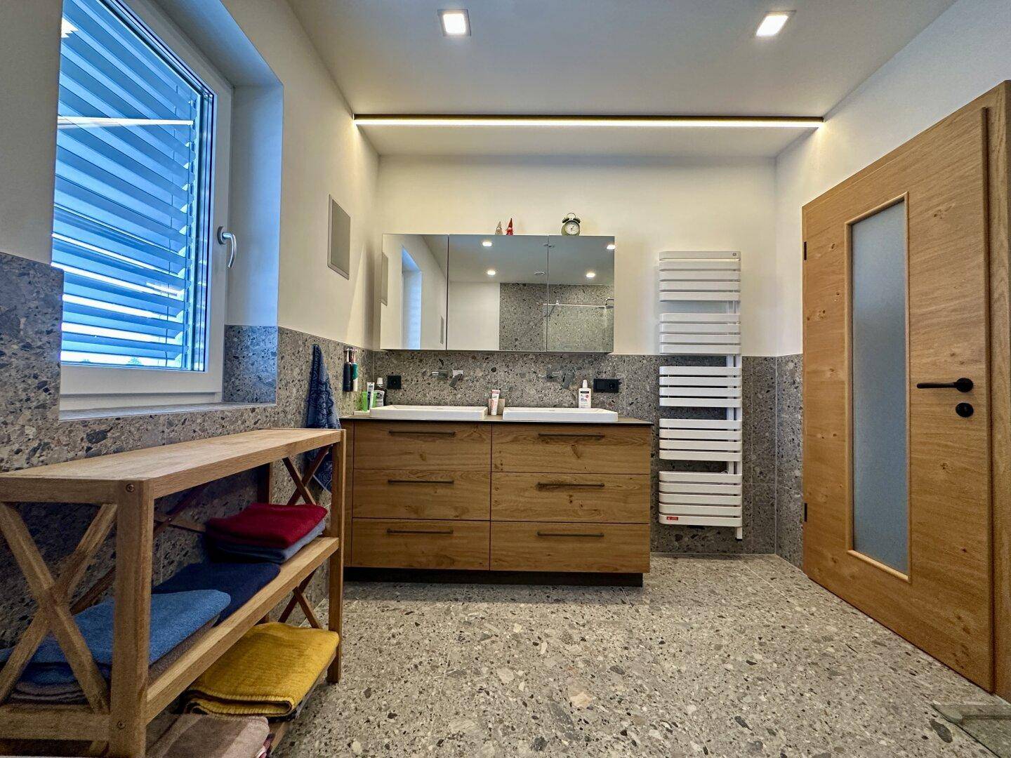 Modernes Badezimmer mit Doppelwaschbecken, grauen Fliesen und beheiztem Handtuchhalter.