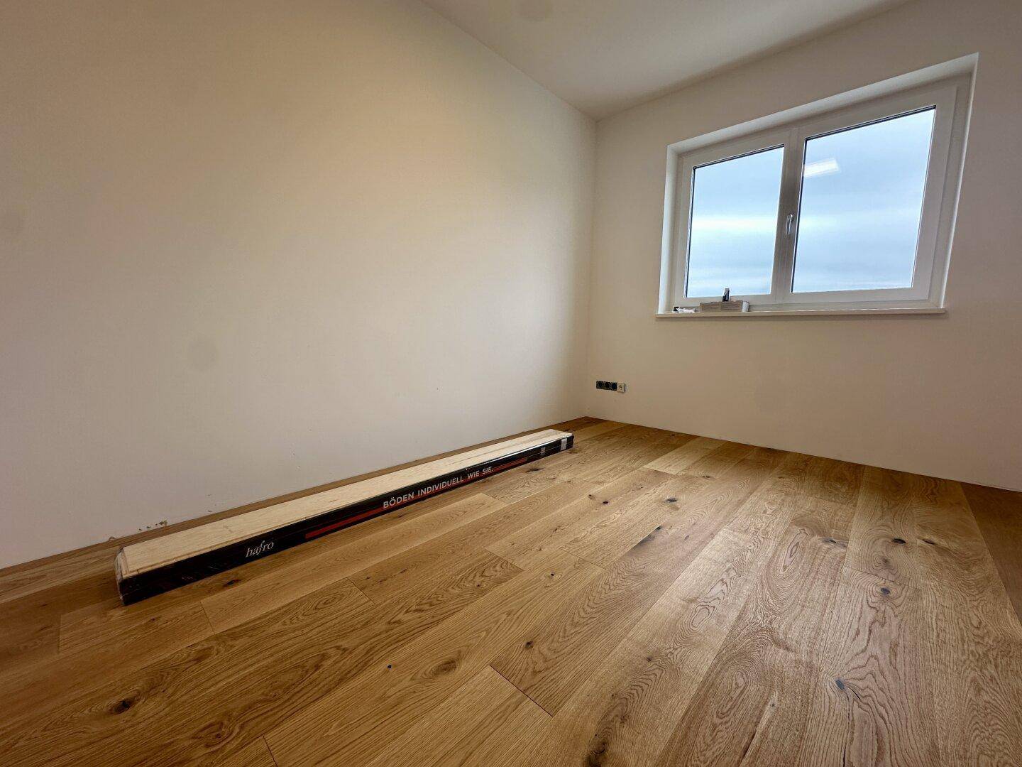 Heller Raum mit Holzboden und Fenster, der auf den Einzug und die Möblierung wartet.