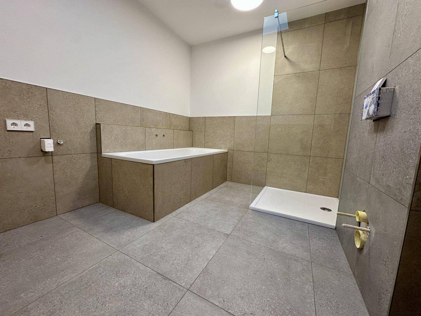 Modernes Badezimmer mit Badewanne, Duschbereich und großformatigen Fliesen an Wänden und Boden.