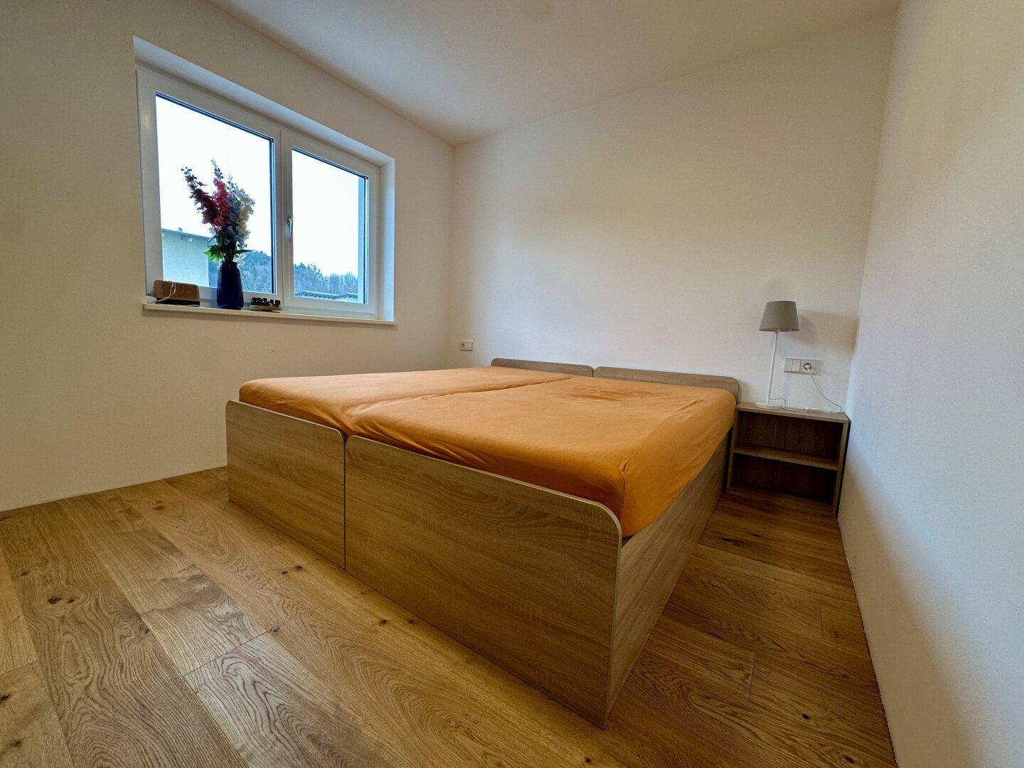 Helles Schlafzimmer mit Holzboden und einem Doppelbett, das auf den Einzug wartet.