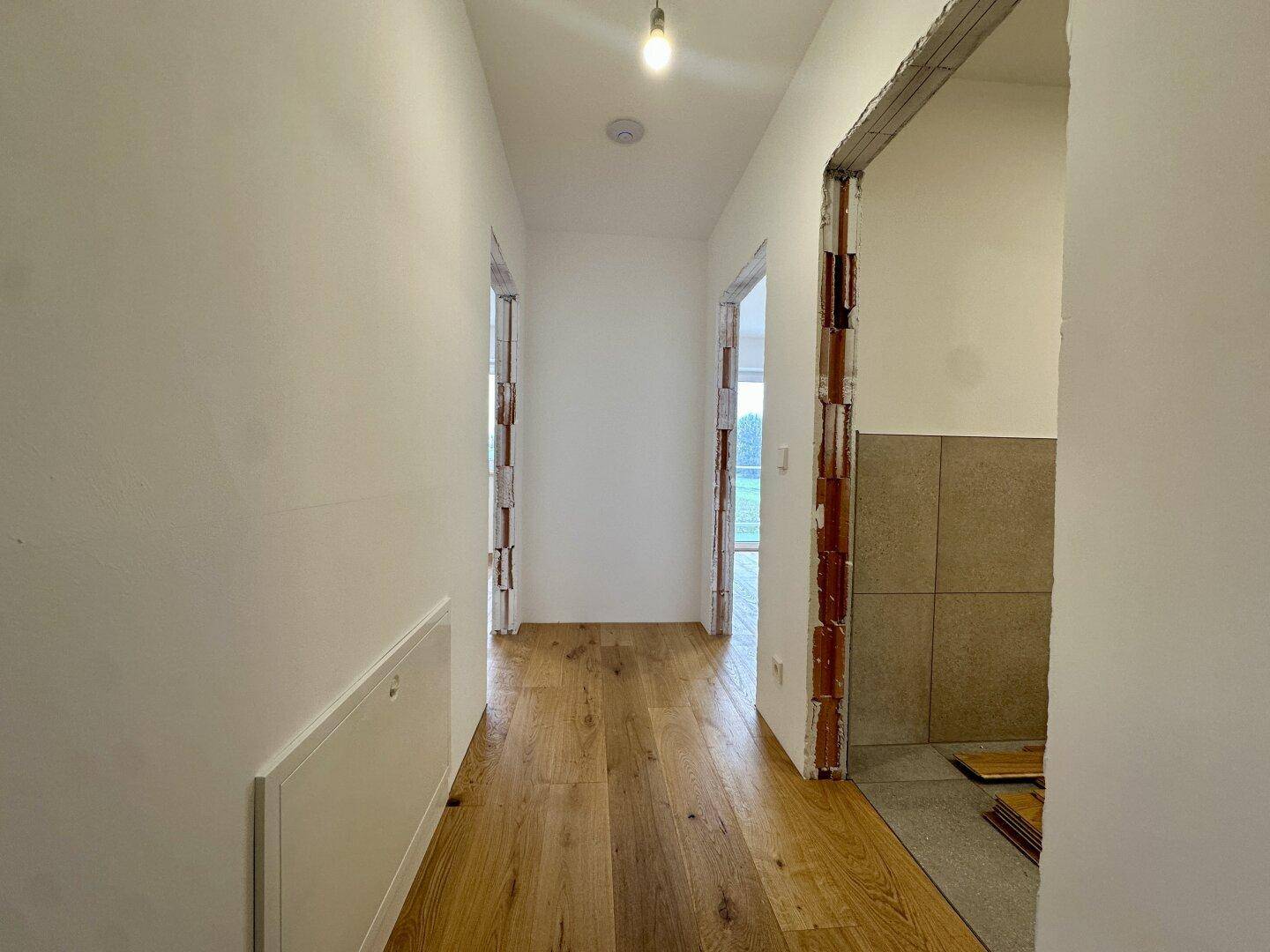 Heller Flur mit Holzboden und offenen Türrahmen, der zu weiteren Räumen führt.