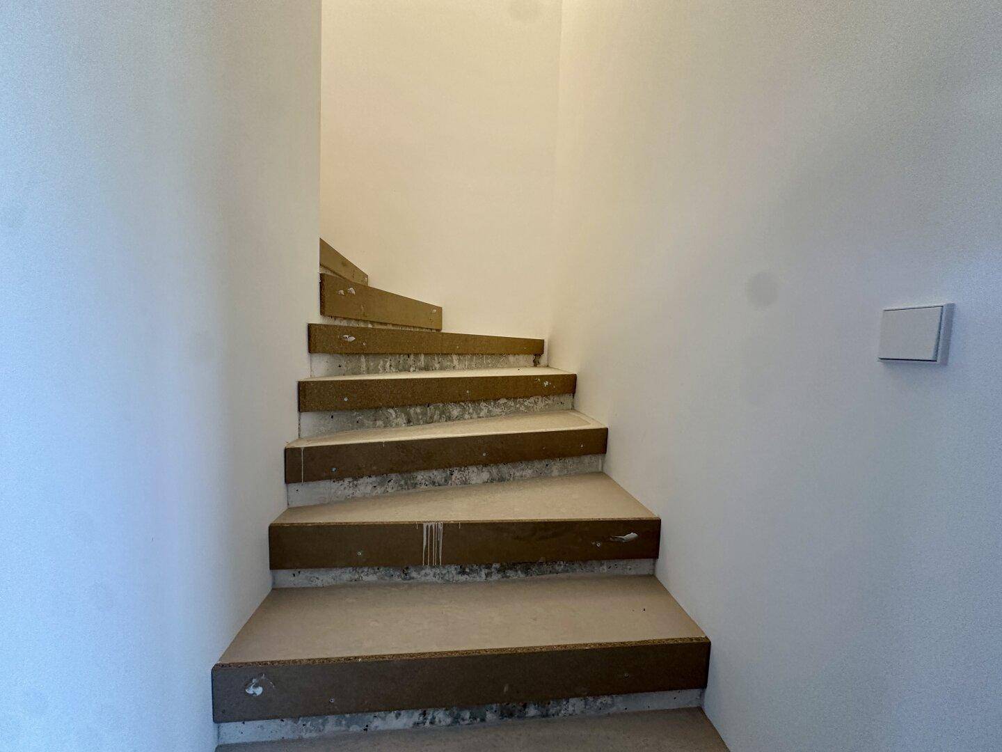 Treppenaufgang im Rohbau mit provisorischen Stufen und weißen Wänden, bereit für den Endausbau.