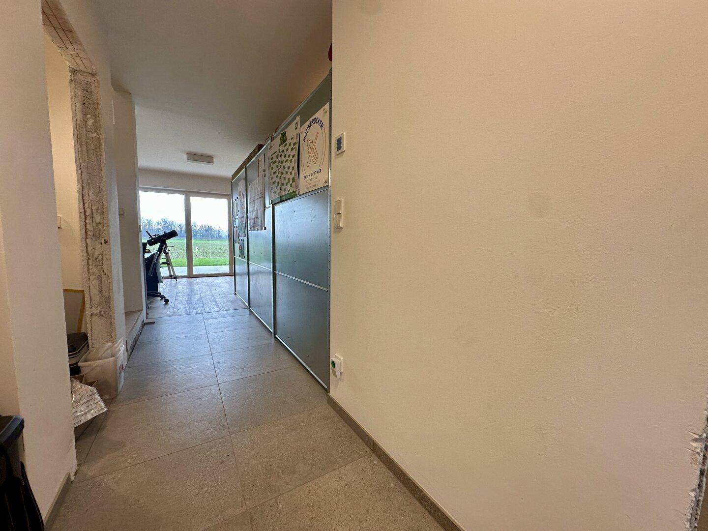 Langer Flur mit Fliesenboden und Blick auf den Garten durch eine große Glastür.