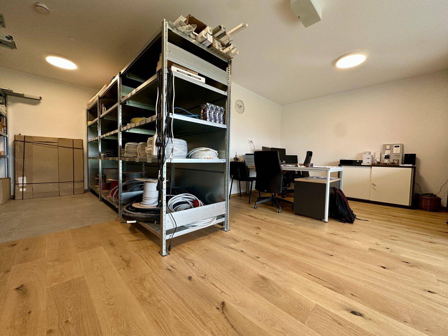 Geräumiger Raum mit Holzboden, Regalen und einem Arbeitsbereich, der als Büro oder Lager dient.