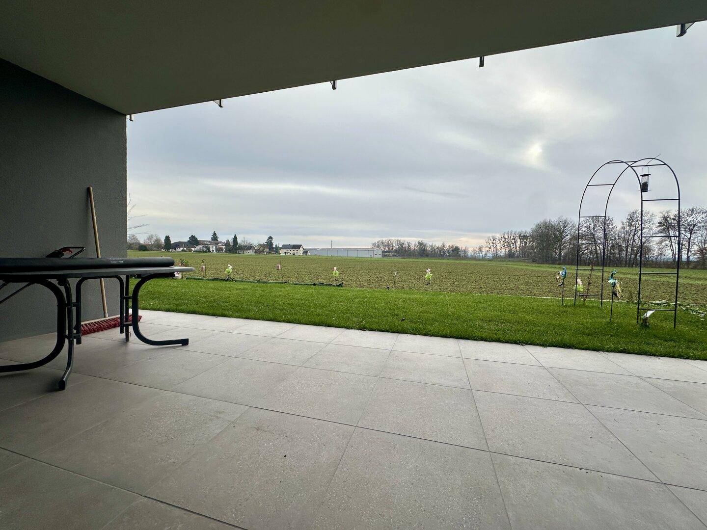 Überdachte Terrasse mit Fliesenboden und Blick auf eine weite grüne Wiese und ländliche Umgebung.