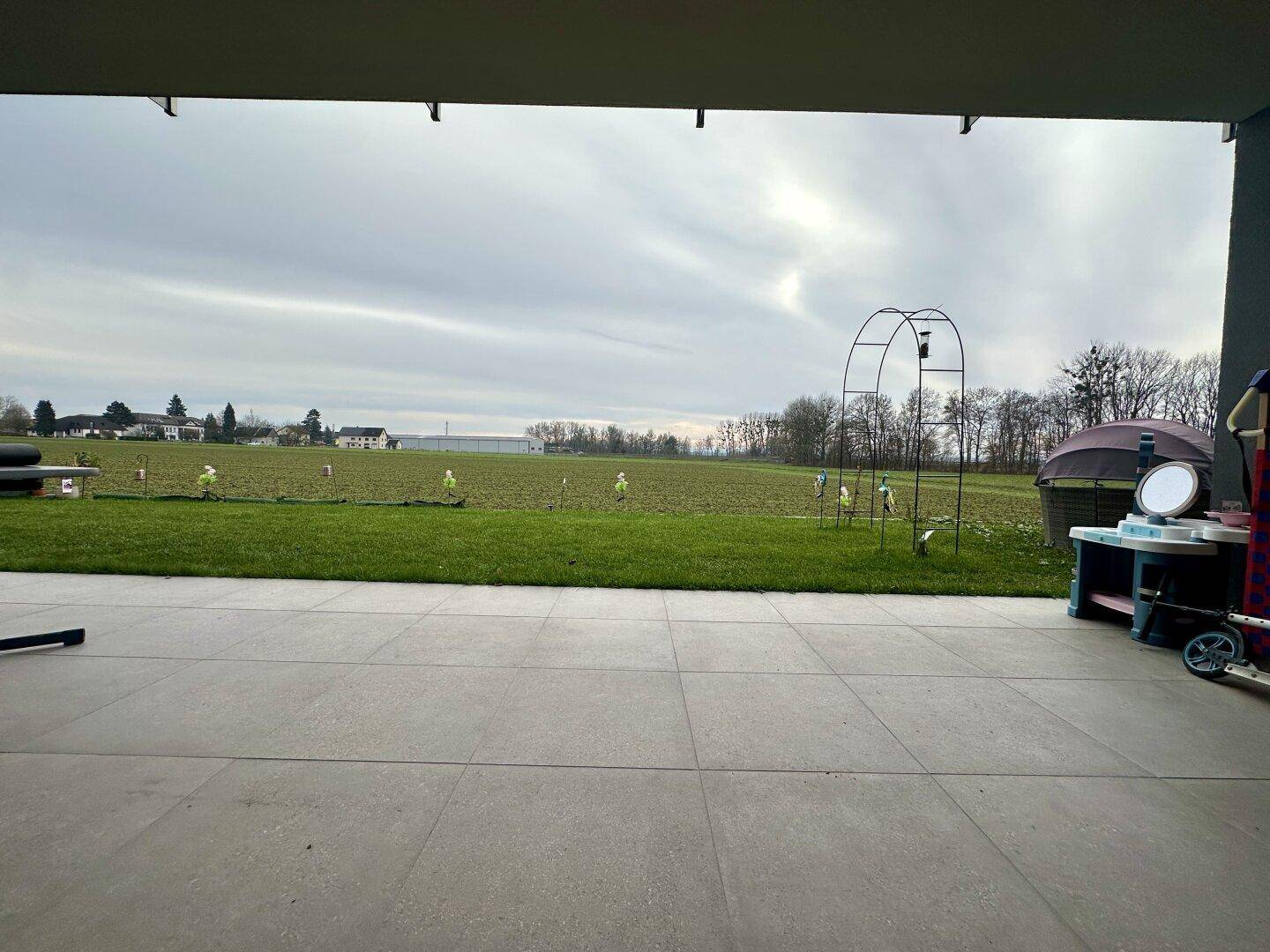 Überdachte Terrasse mit Fliesenboden und Blick auf eine weite grüne Wiese und ländliche Umgebung.