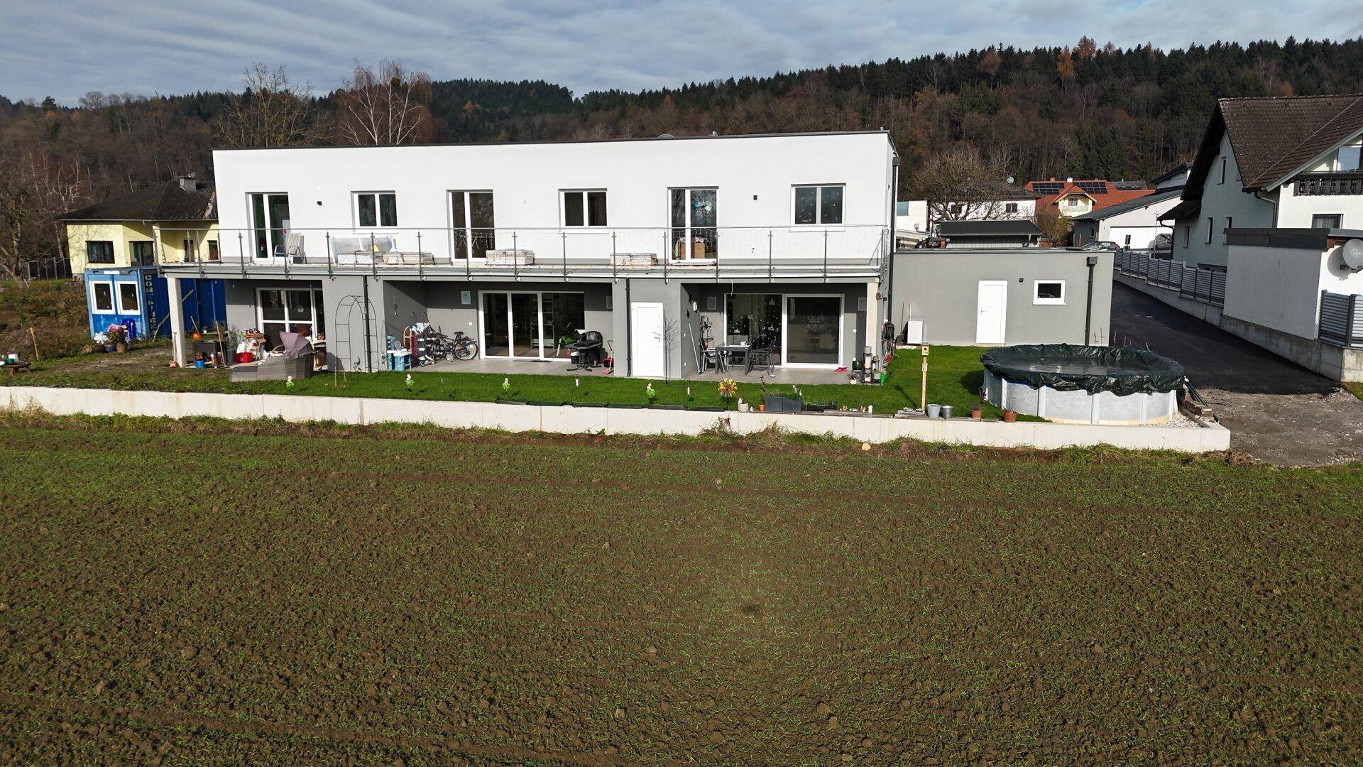 Rückansicht eines modernen Reihenhauses mit Terrassen, Balkonen und einem Aufstellpool im Garten.