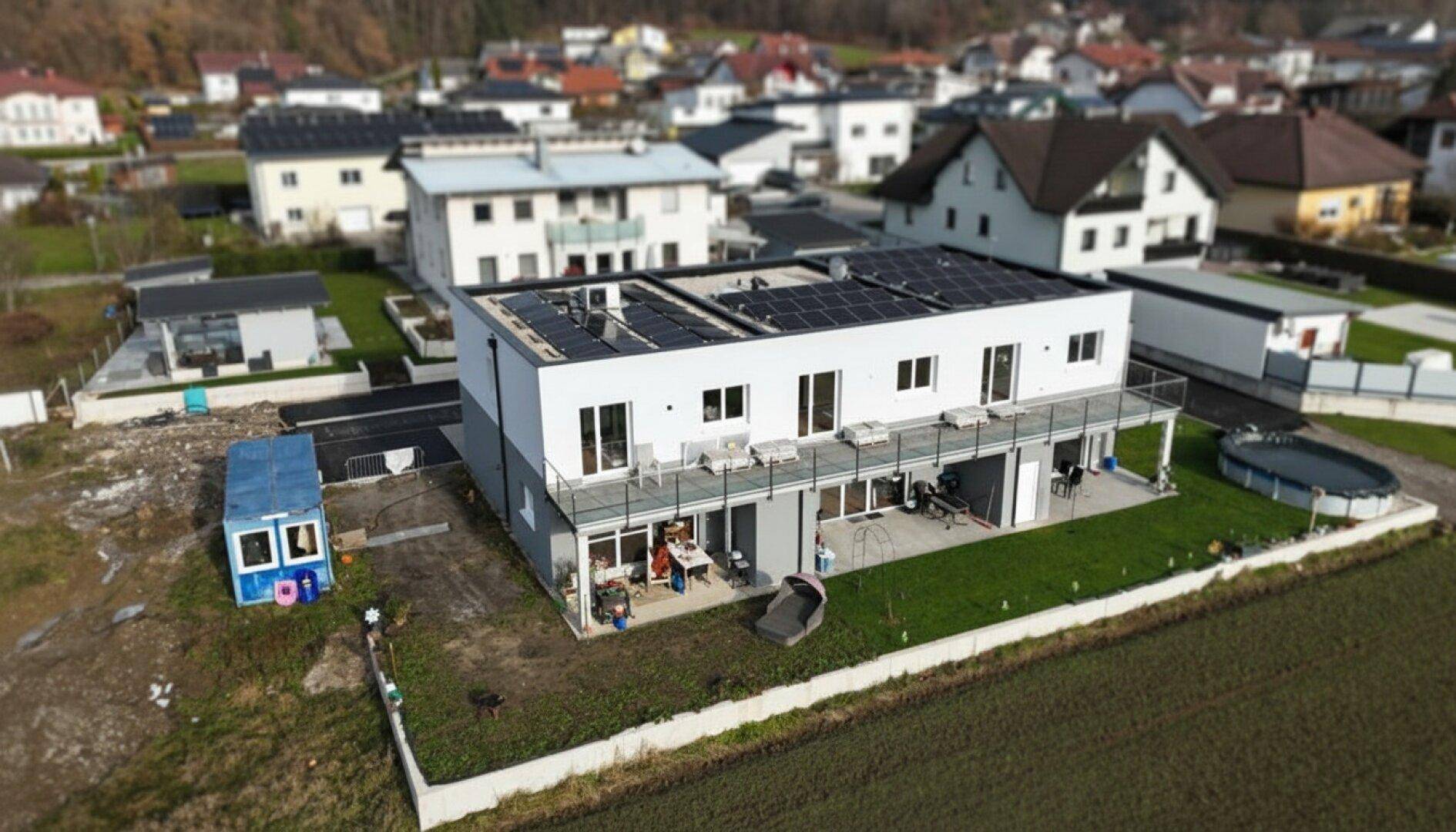 Luftaufnahme einer modernen Reihenhaussiedlung mit Photovoltaikanlage auf dem Dach und ländlicher Umgebung.