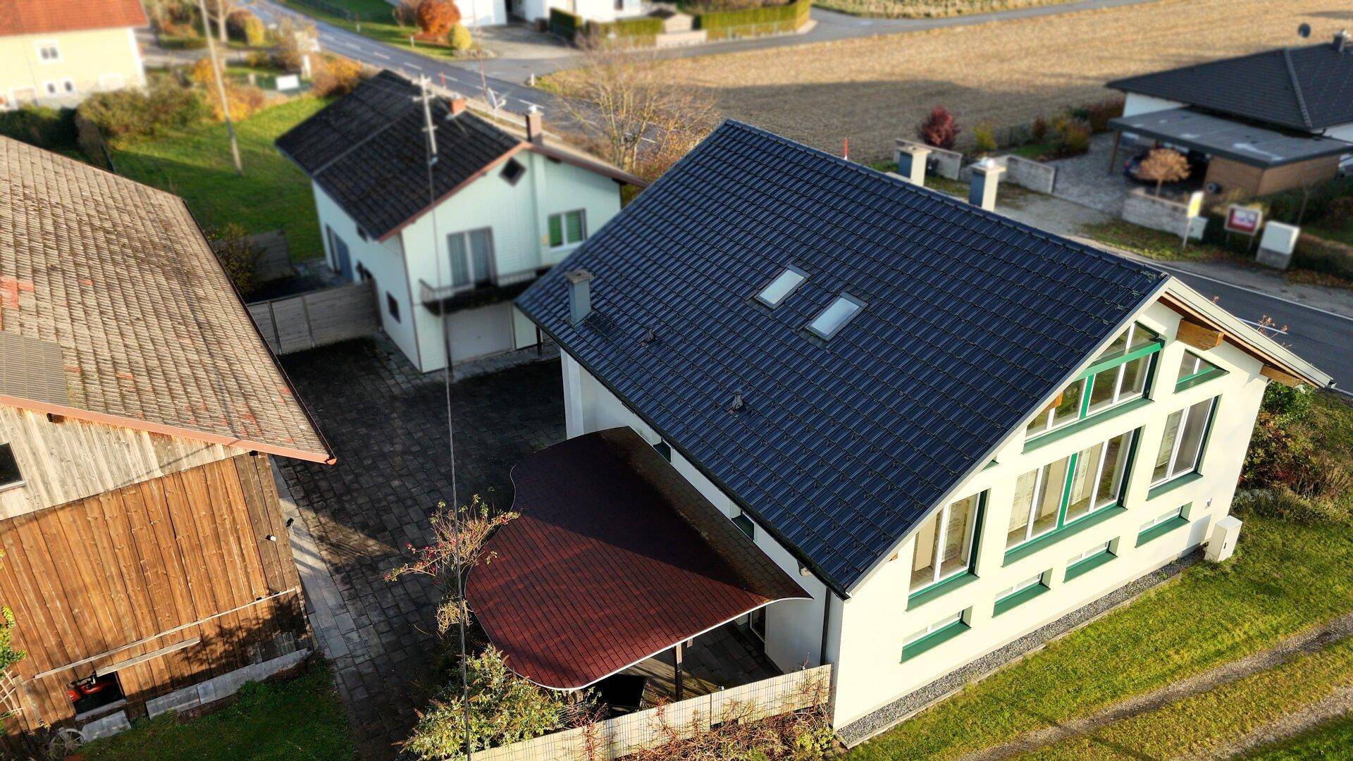 Luftaufnahme des Wohnhauses mit dunklem Dach, Dachfenstern und einer überdachten Terrasse.