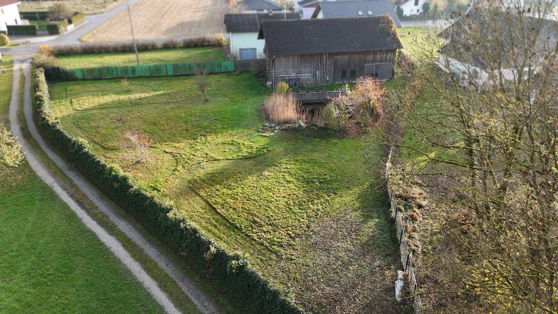 Luftaufnahme des weitläufigen Grundstücks mit Hecke, Feldweg und angrenzender Scheune.