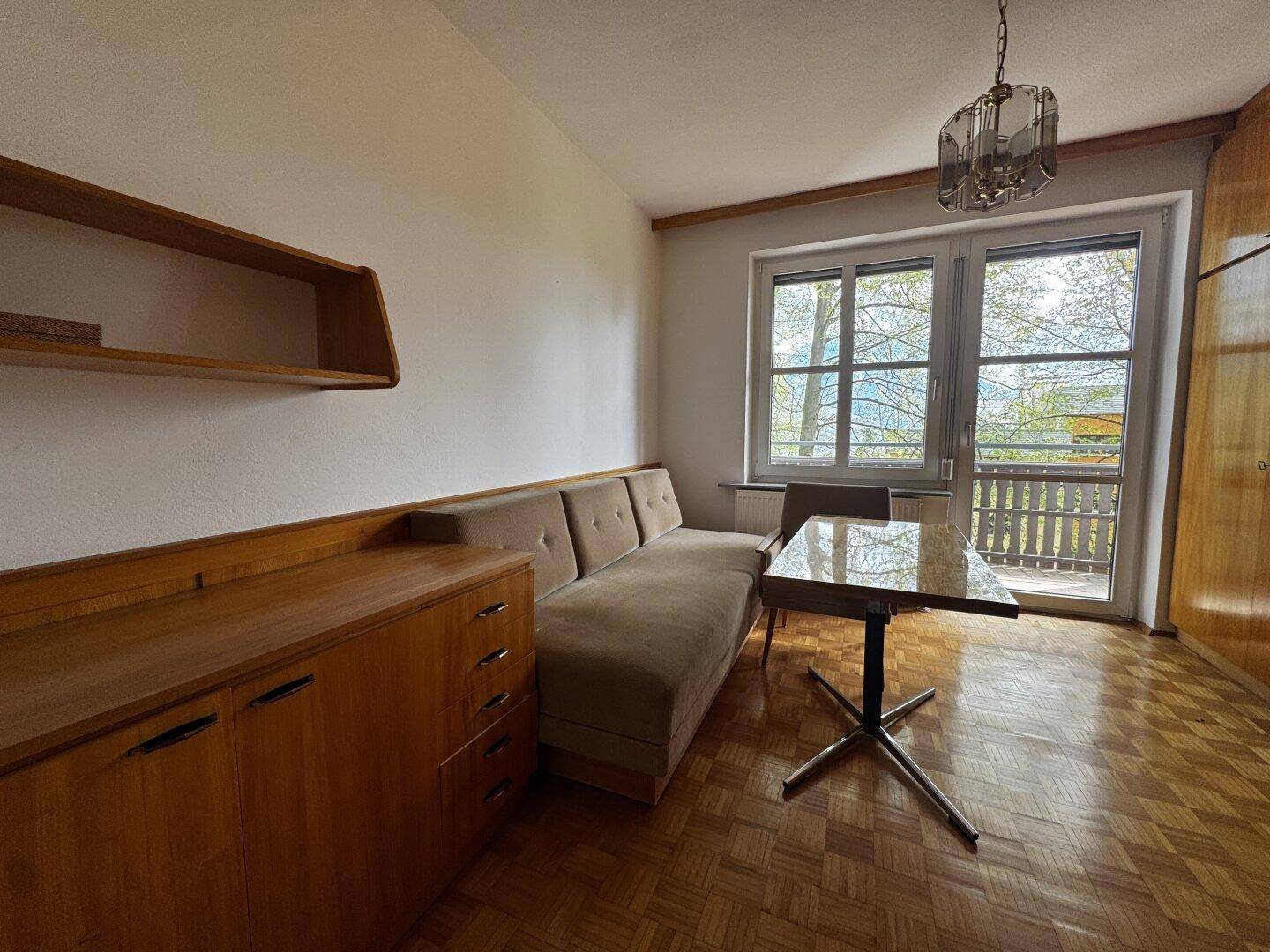 Schlafzimmer mit Parkettboden, Schrank und Zugang zum Balkon mit Aussicht.