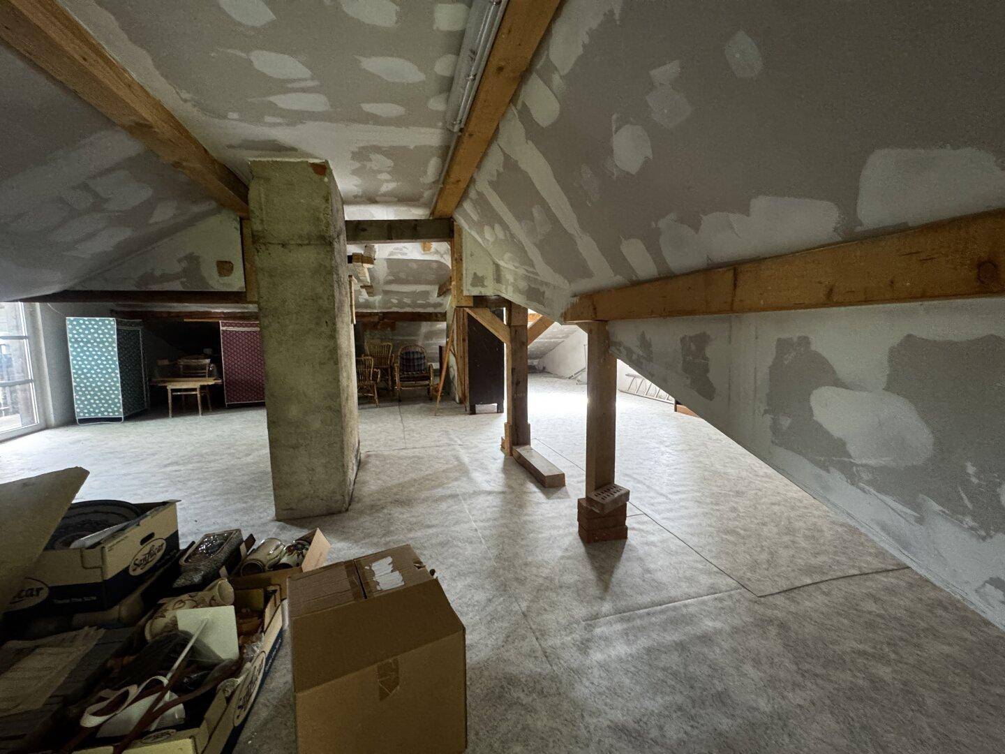 Unausgebauter Dachboden mit sichtbaren Holzbalken und Trockenbauwänden, bietet Ausbaupotenzial.