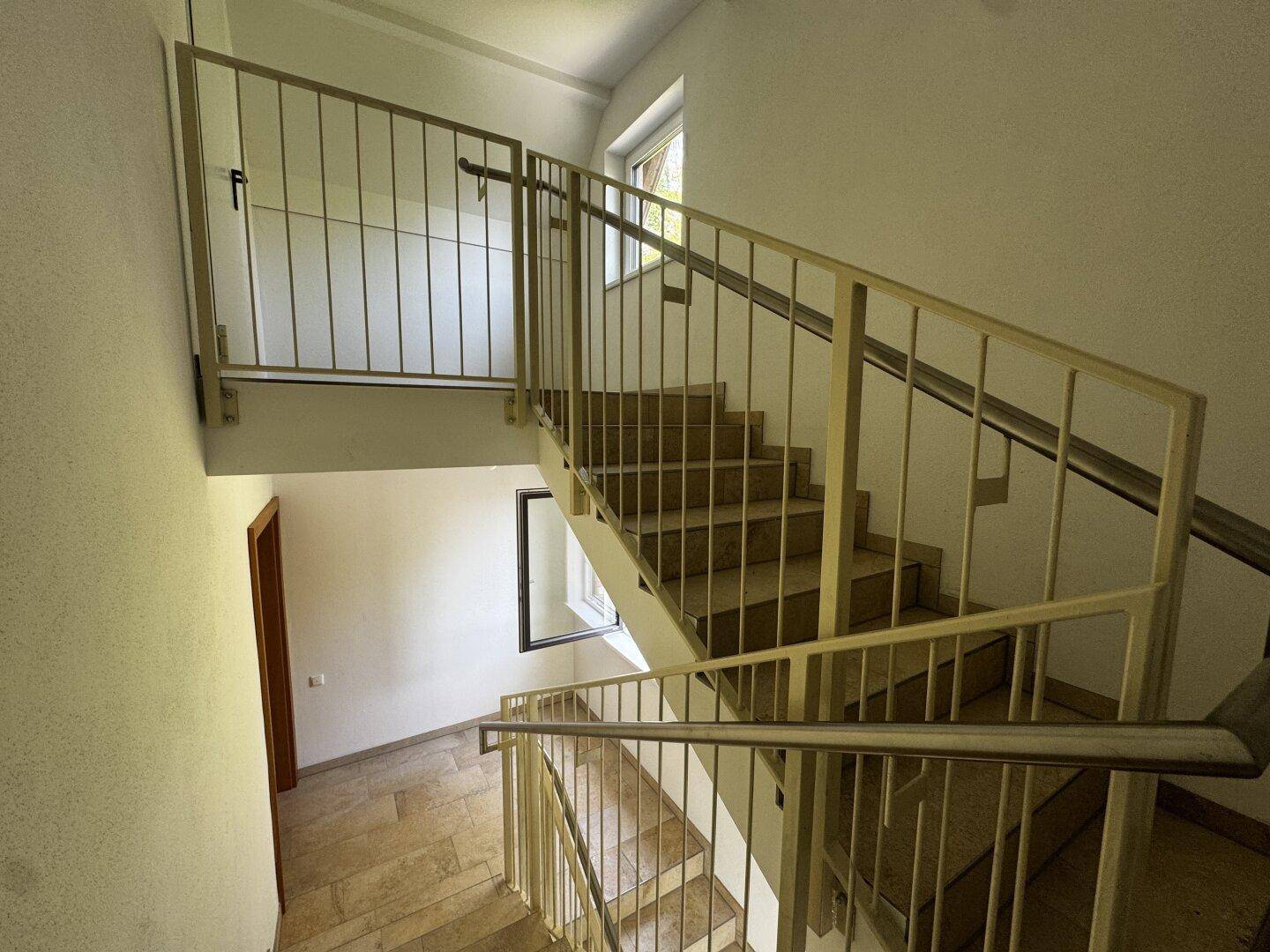 Geräumiger Treppenaufgang mit Metallgeländer und Fenstern, die Tageslicht hereinlassen.