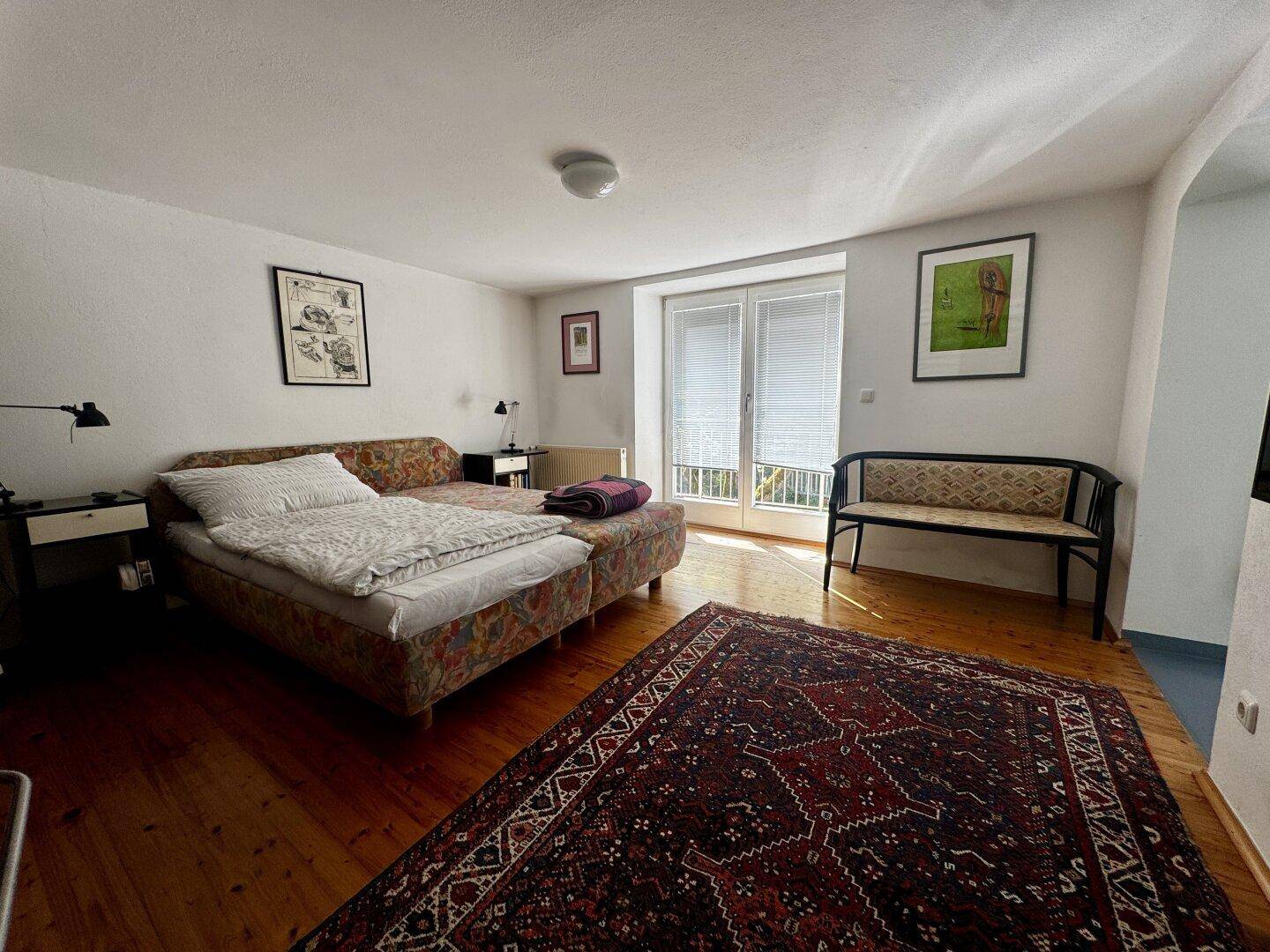 Helles Schlafzimmer mit Holzboden, großem Bett und Zugang zu einem französischen Balkon.
