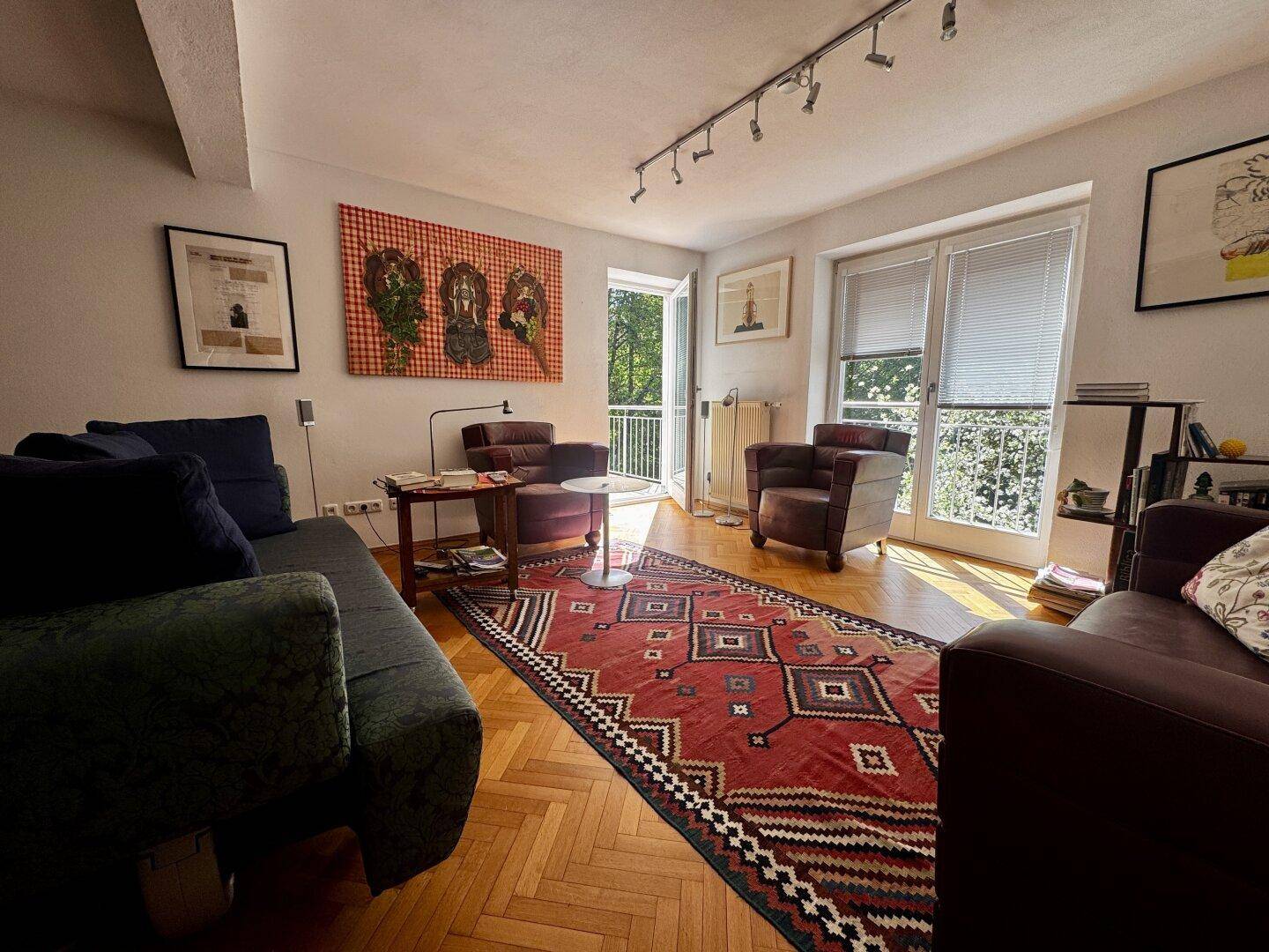 Gemütliches Wohnzimmer mit Fischgrätparkett, bequemen Sofas und Zugang zum Balkon.