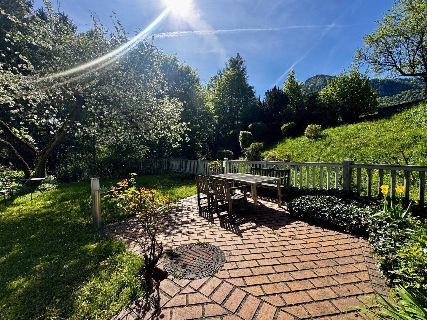 Sonniger Terrassenbereich im Garten mit Esstisch und Blick auf die grüne Umgebung.