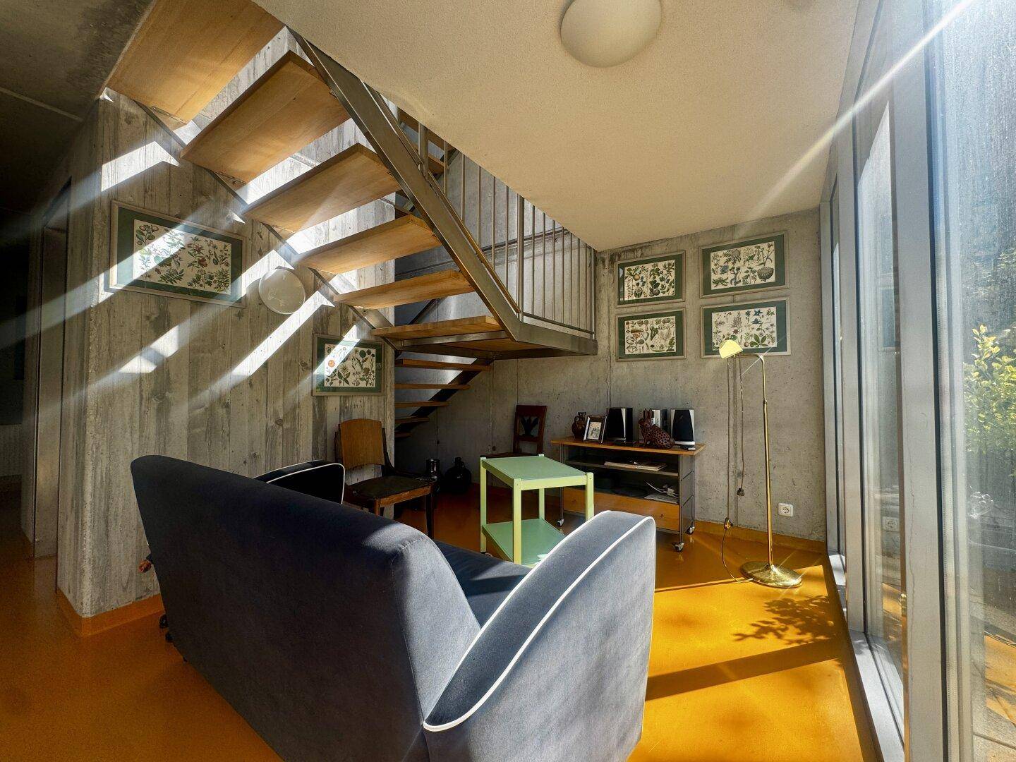 Offener Wohnbereich mit Treppe, gelbem Boden und viel Tageslicht durch die Fensterfront.