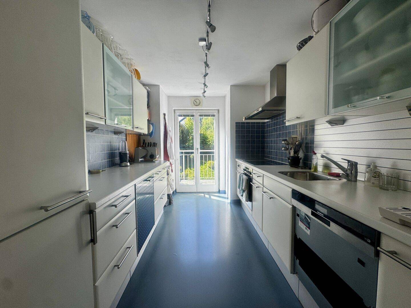 Funktionale Küche mit weißen Schränken, blauen Fliesen und Zugang zu einem kleinen Balkon.