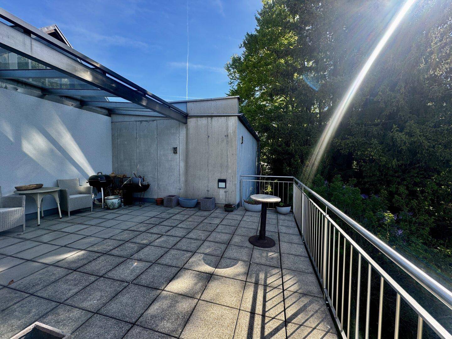 Große Dachterrasse mit Fliesenboden, Grillbereich und teilweiser Überdachung, ideal für Entspannung.