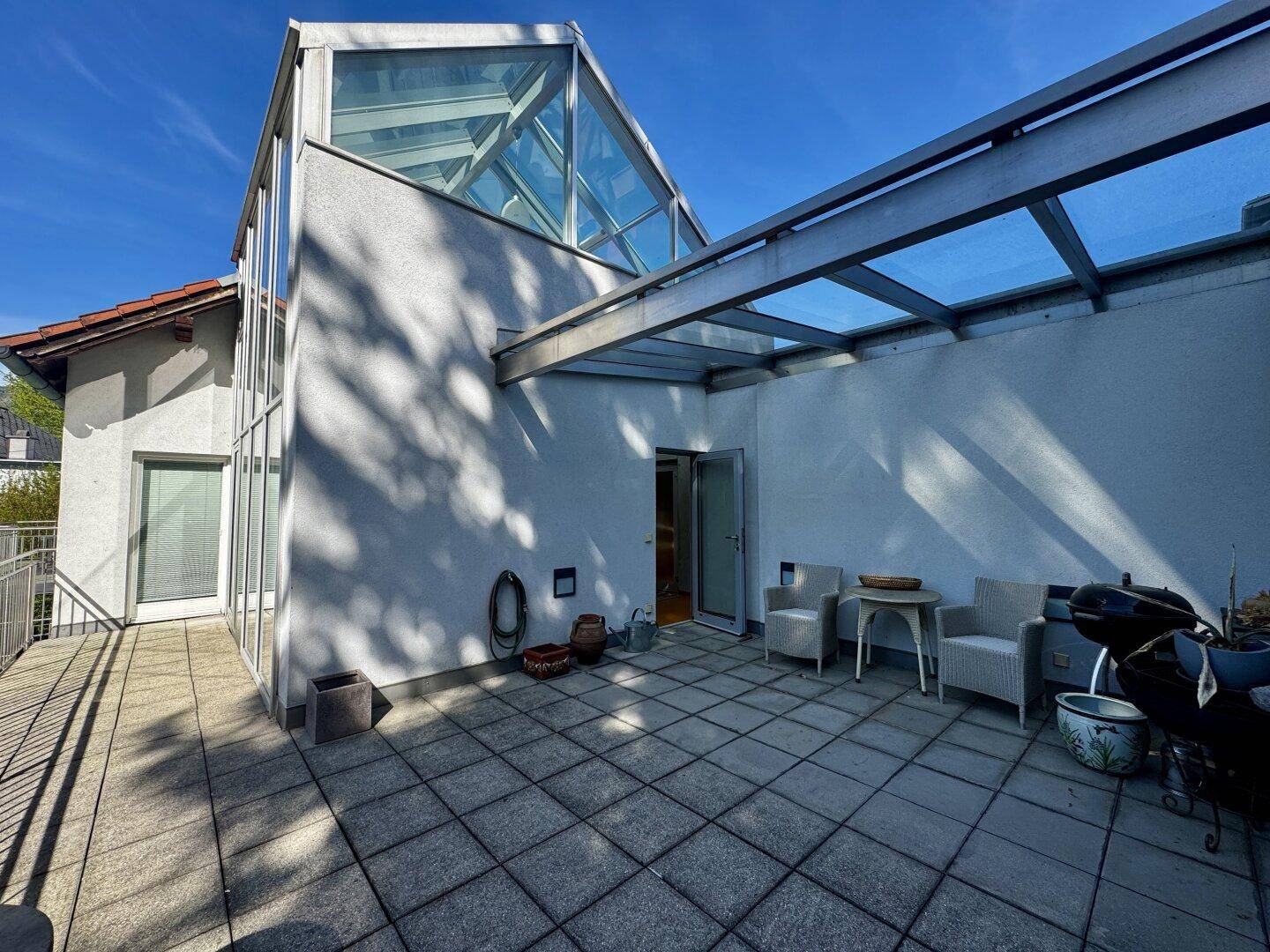 Weitläufige Terrasse mit moderner Architektur, Glasüberdachung und Sitzgelegenheiten im Freien.
