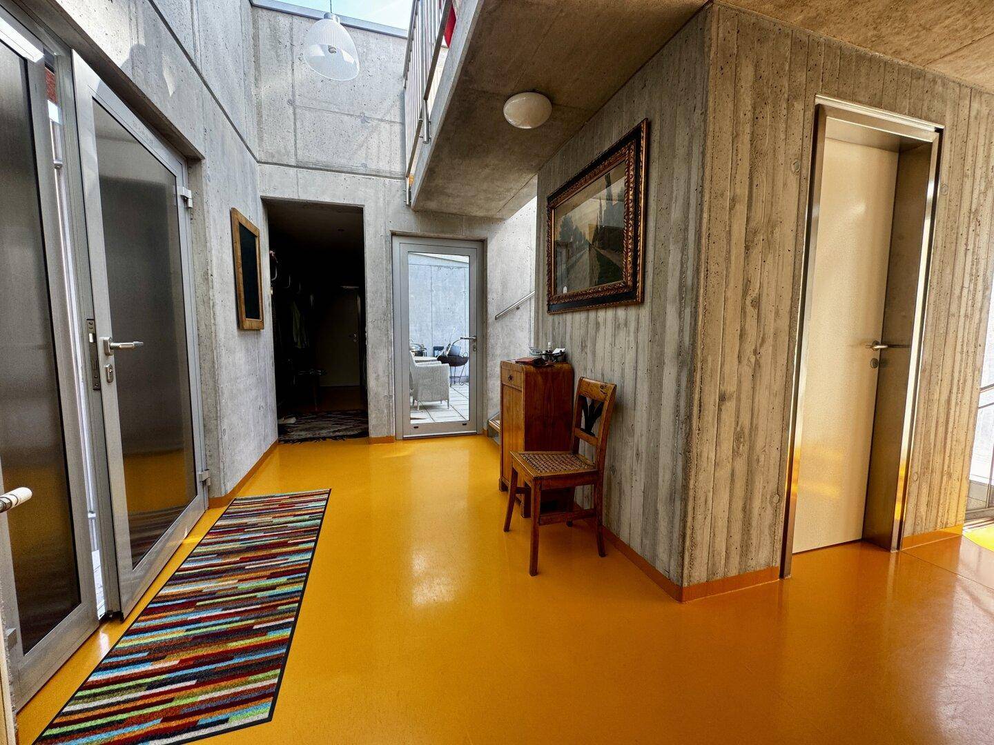 Moderner Eingangsbereich mit gelbem Boden, Sichtbeton und Kunstwerken an den Wänden.