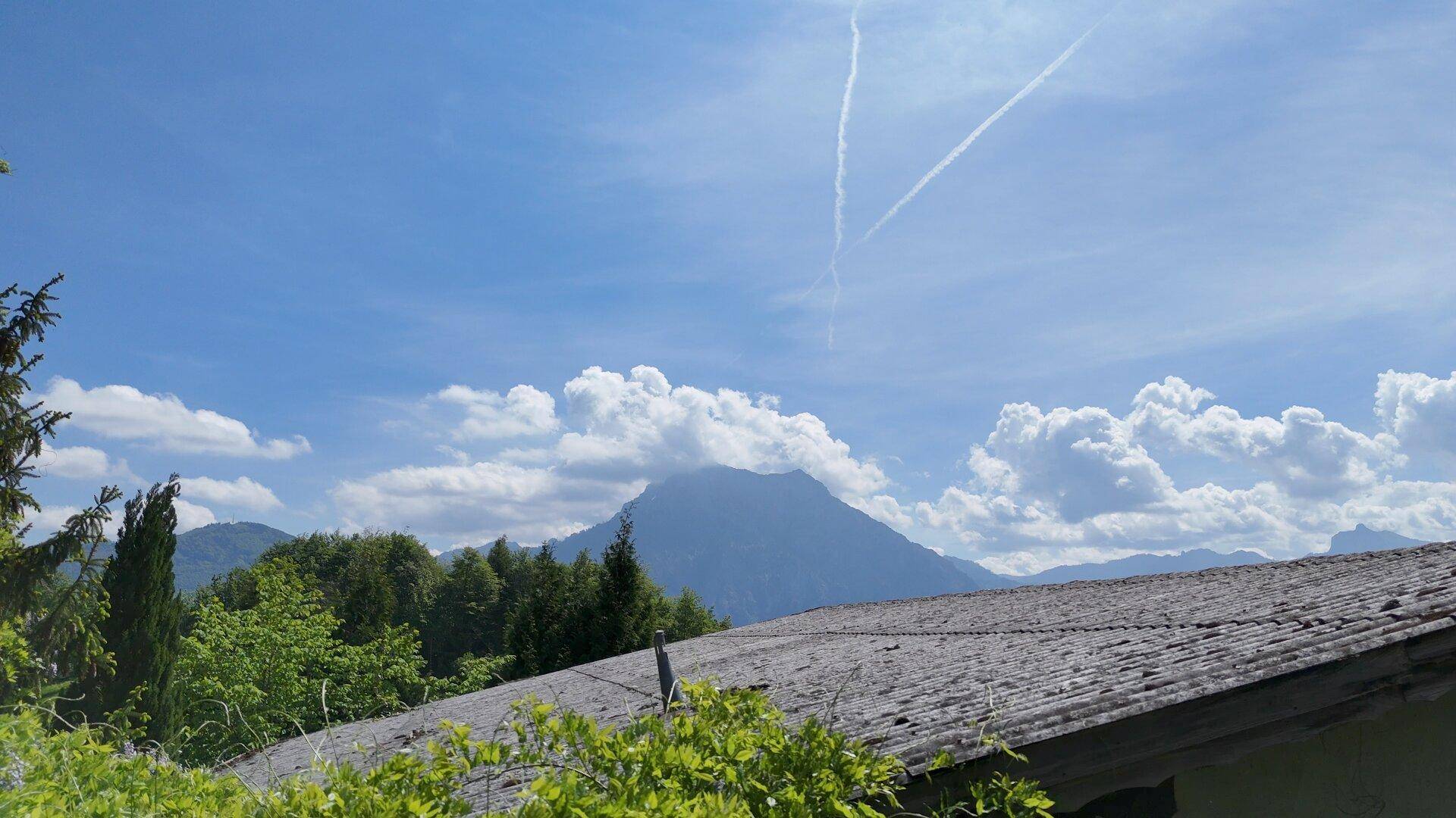 Panoramablick über ein Hausdach auf majestätische Berge unter einem weiten blauen Himmel.