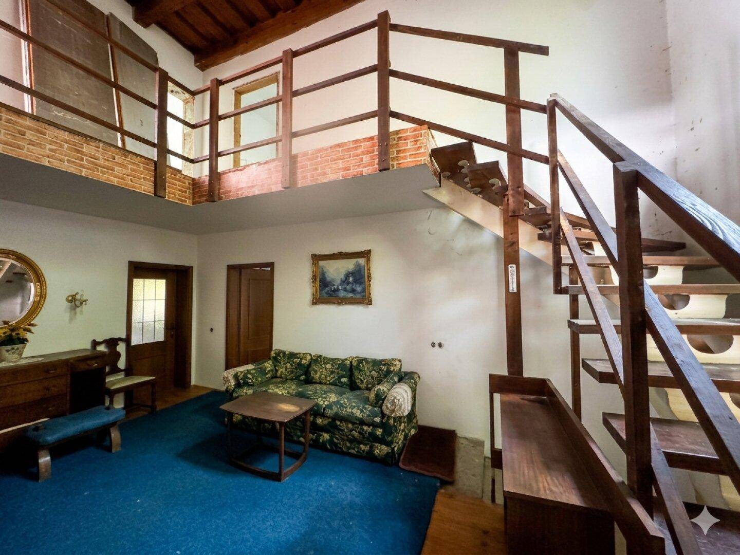 Gemütliches Wohnzimmer mit Sofa, Holztreppe und sichtbaren Deckenbalken, die rustikal wirken.