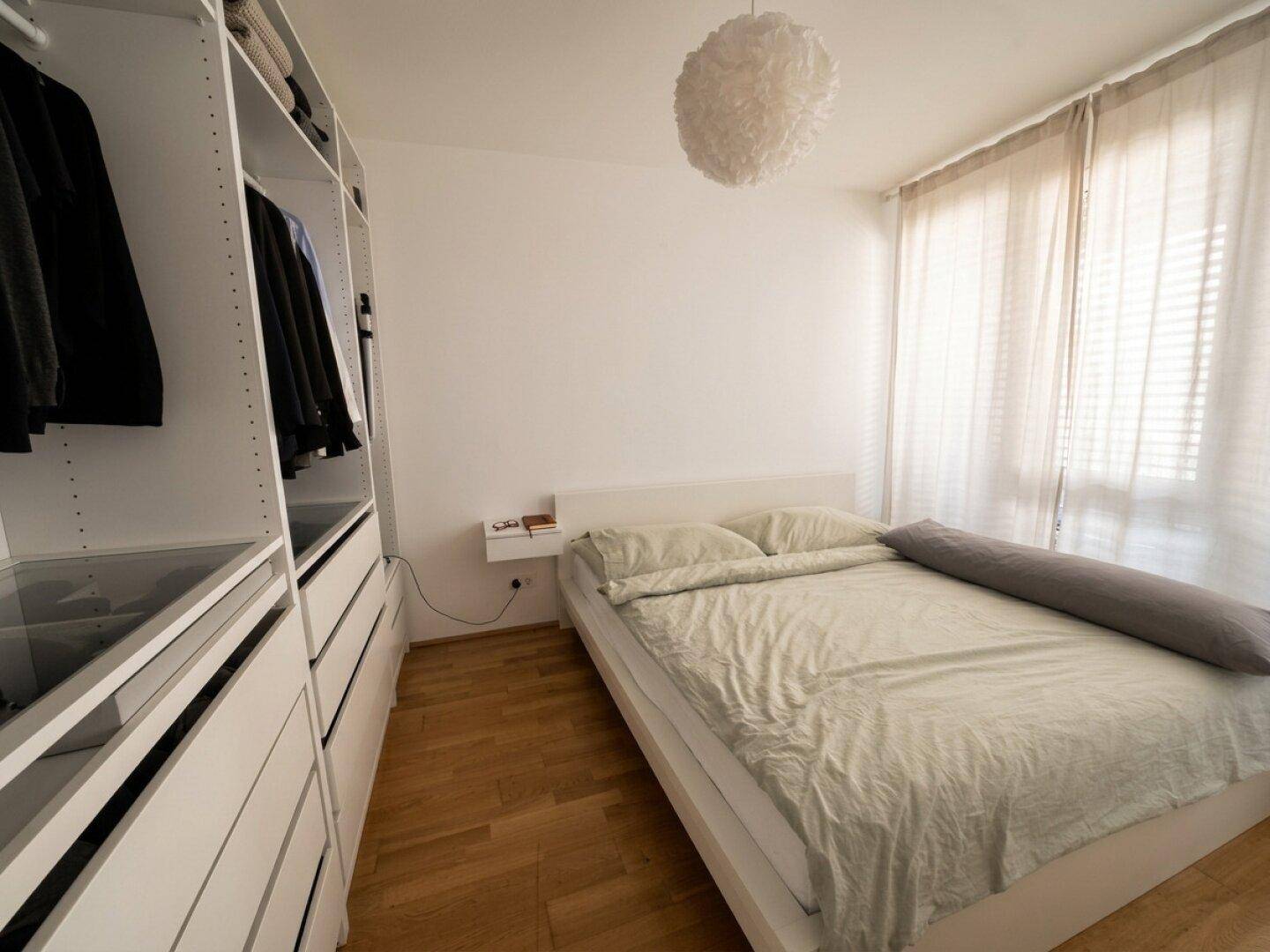 Schlafzimmer mit Doppelbett, integriertem Kleiderschrank und hellem Holzboden.