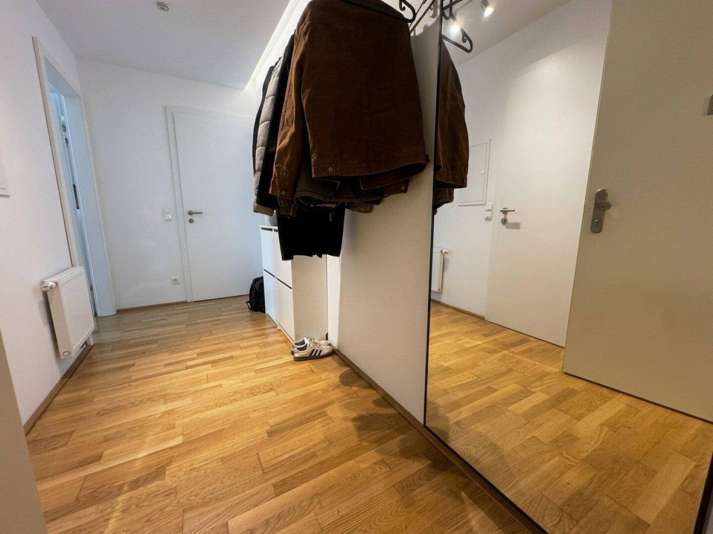 Heller Flur mit Holzboden, Garderobe und großem Spiegel.