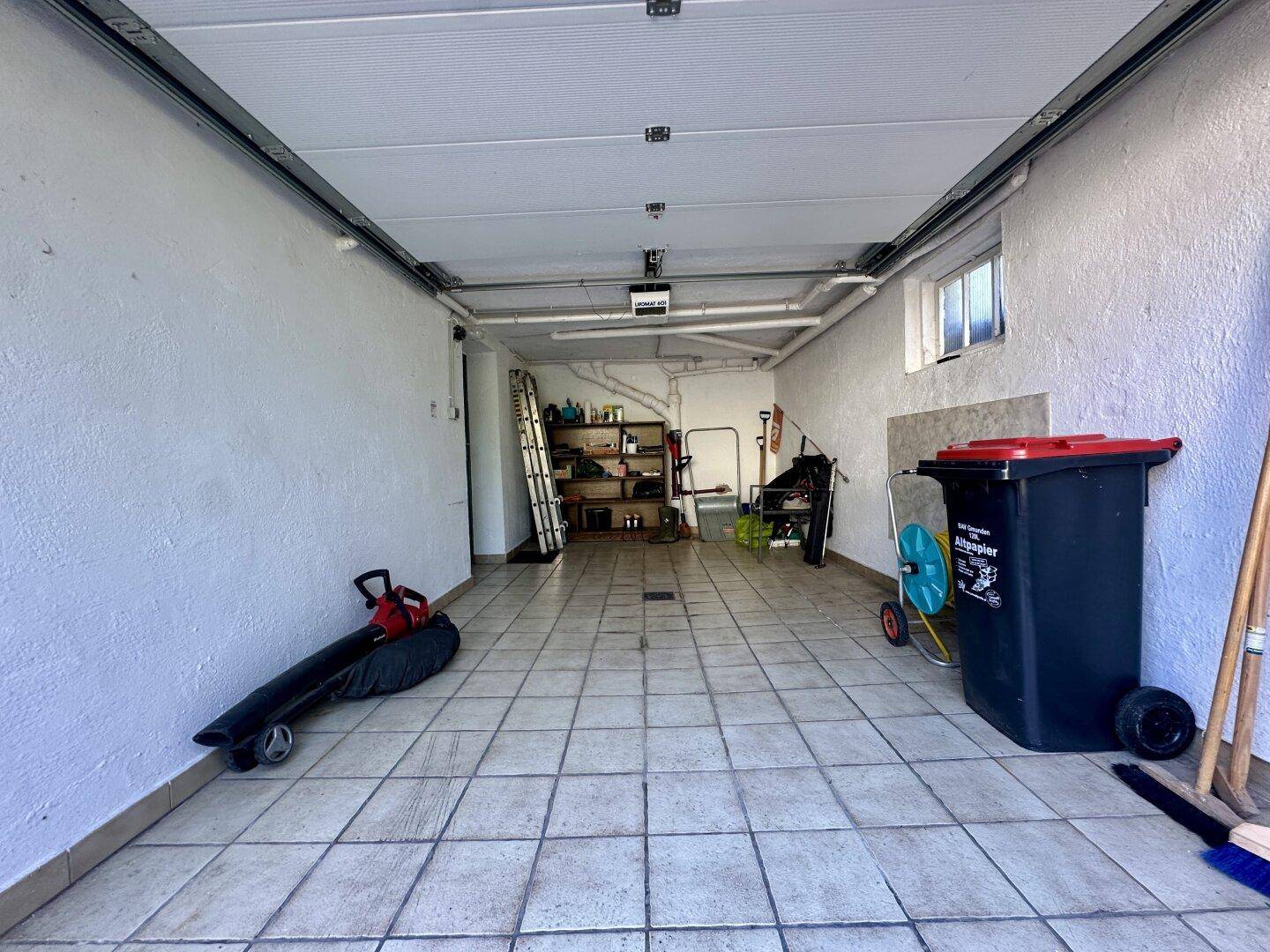 Geräumige Garage mit Fliesenboden, Stauraum und Rolltor.