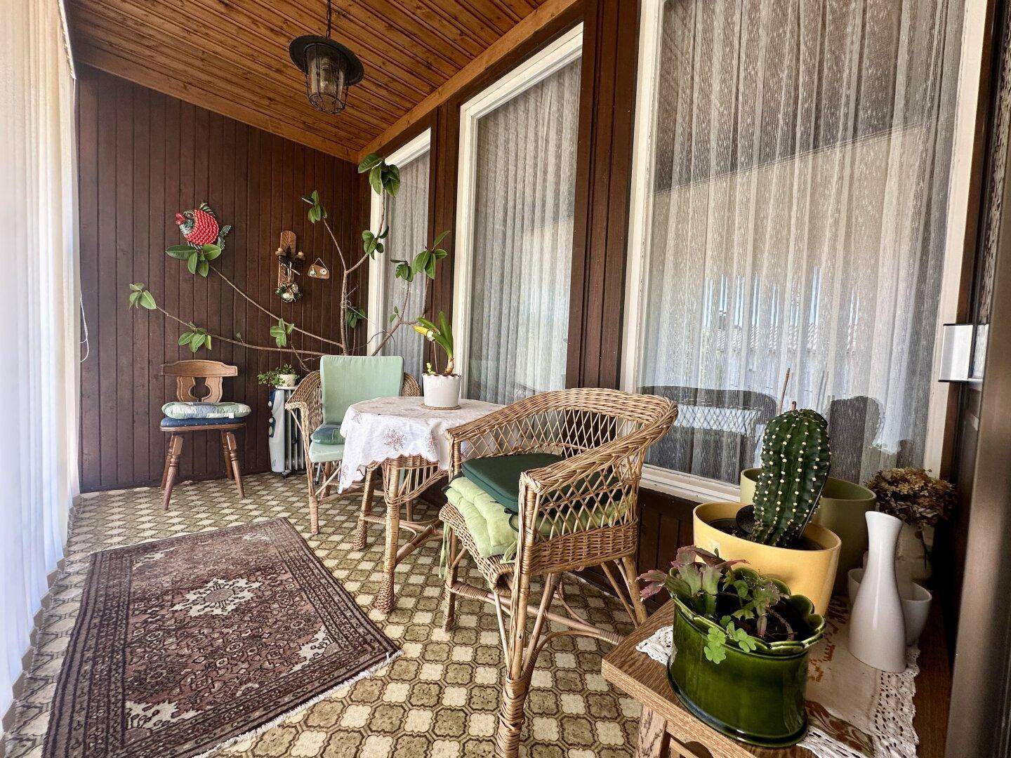 Gemütlicher Wintergarten mit Korbmöbeln, Holzvertäfelung und Blick ins Grüne.