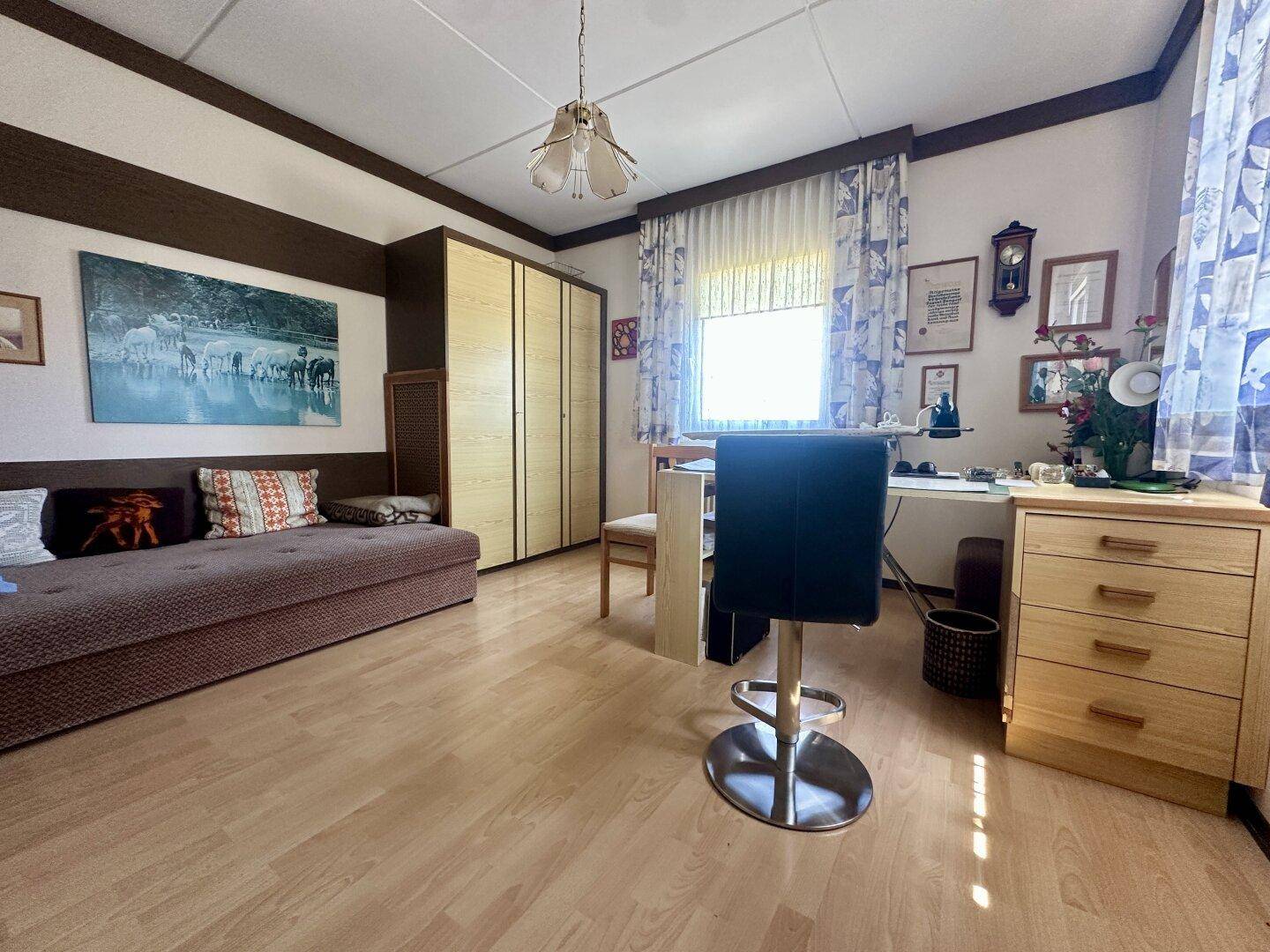 Helles Schlafzimmer mit Laminatboden, Schrankwand und Schreibtischbereich.