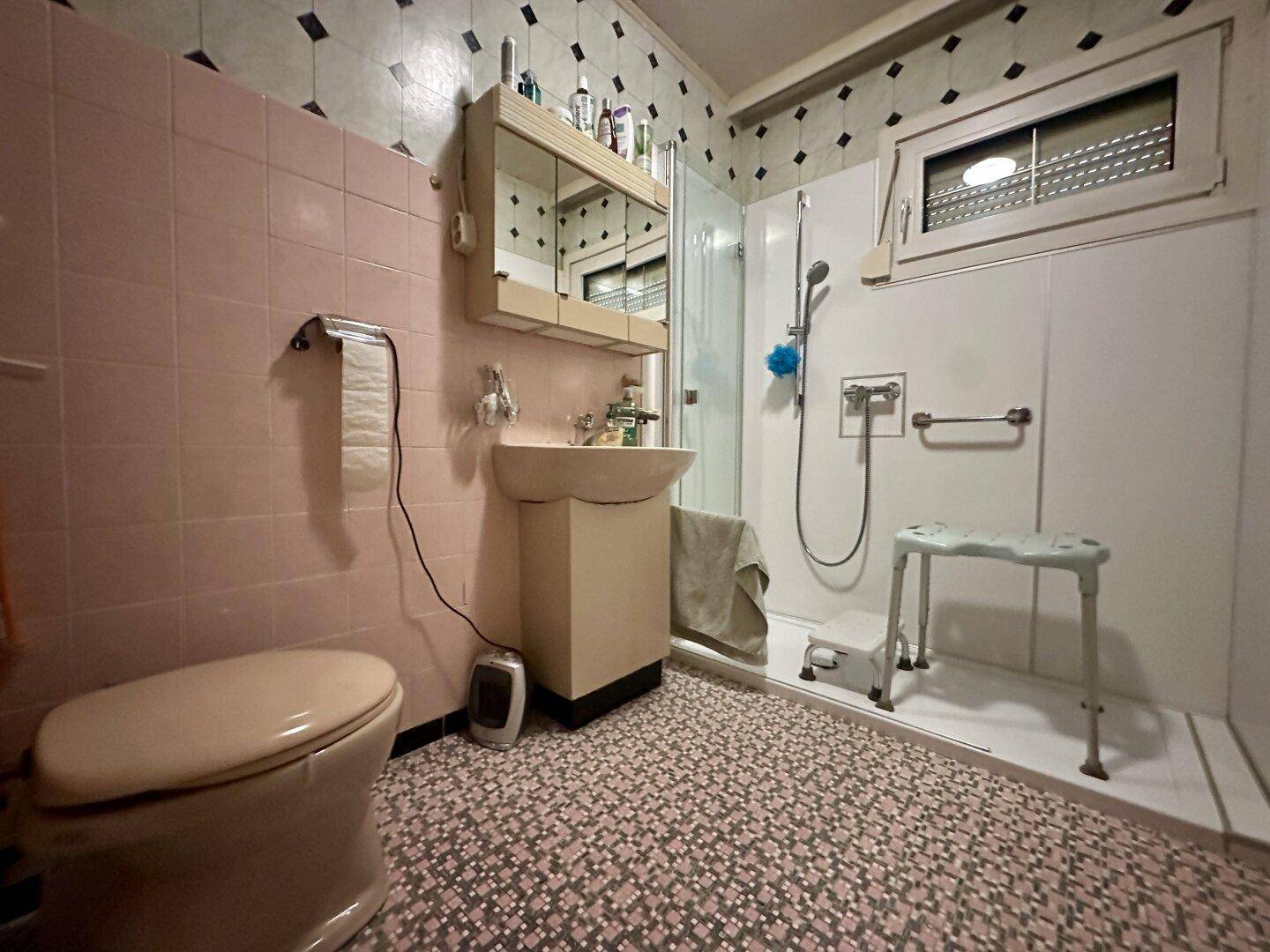 Badezimmer im Stil der 80er Jahre mit rosa Fliesen, Dusche und WC.