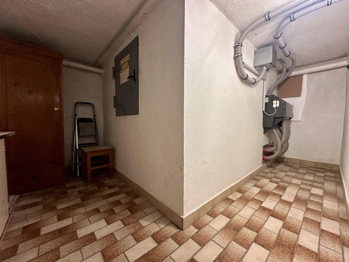 Technikraum mit Fliesenboden, Leitungen und Schaltschrank.